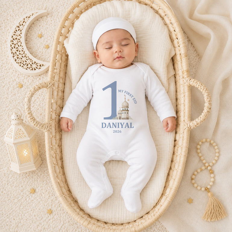 Baby in a white onesie with blue text, lying in a woven basket on a soft beige surface.