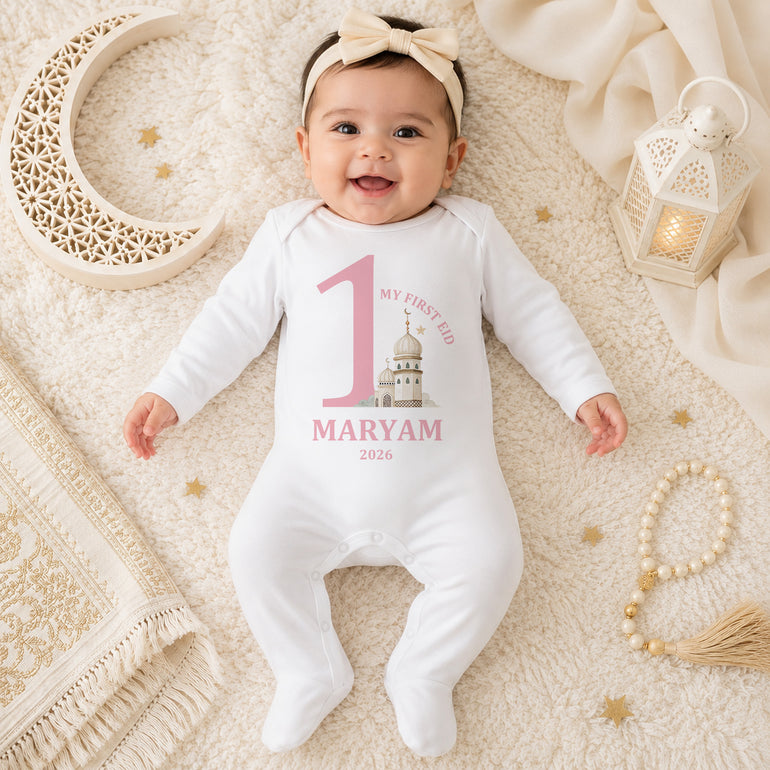 Baby wearing a personalised 1st Eid baby grow with large number one, mosque illustration, name and year in a pink or blue design.