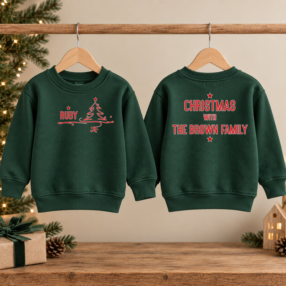 Two forest green family Christmas jumpers, the front with a Christmas tree and the name Ruby, the back reading Christmas with The Brown Family