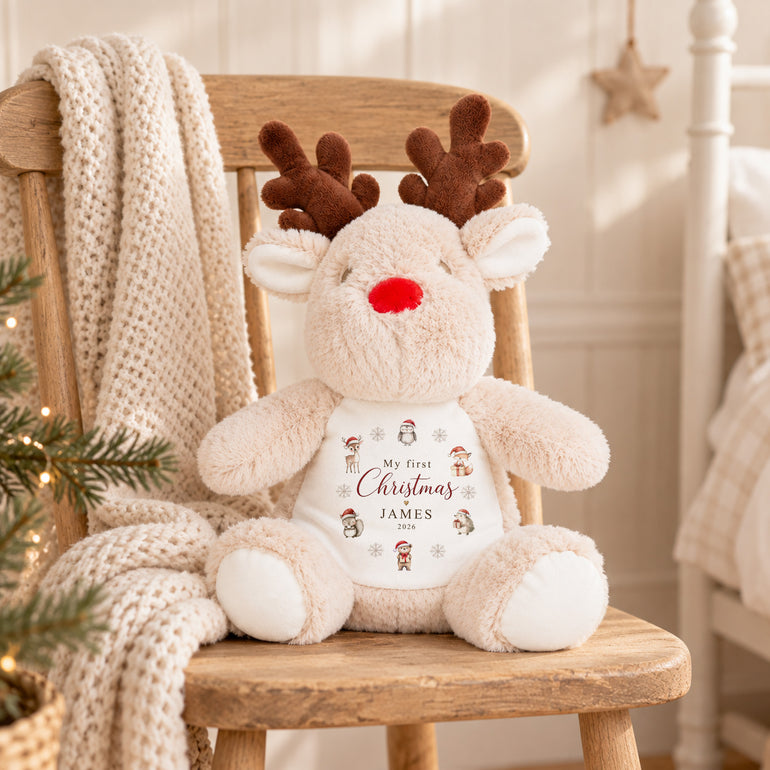 Cream personalised reindeer soft toy with My First Christmas woodland design, example name James and year 2026 displayed on a wooden chair