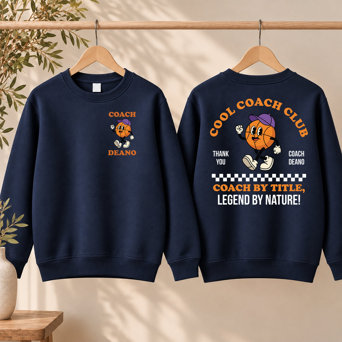 Navy Cool Coach Club basketball coach gift sweatshirt on a hanger, the back printed with Cool Coach Club, a retro cartoon basketball character in a purple cap, Thank You, Coach Deano and Coach by Title, Legend by Nature, the front with a small Coach Deano badge
