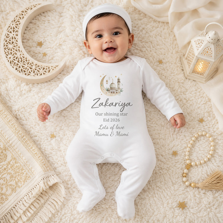 Baby wearing a white BABY GROW with personalized text and design, lying on a soft surface.