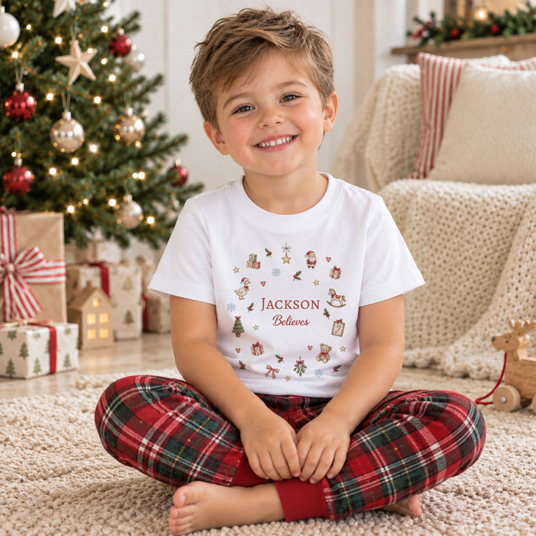Personalised kids Christmas T-shirt with custom name and Believes design worn beside a Christmas tree