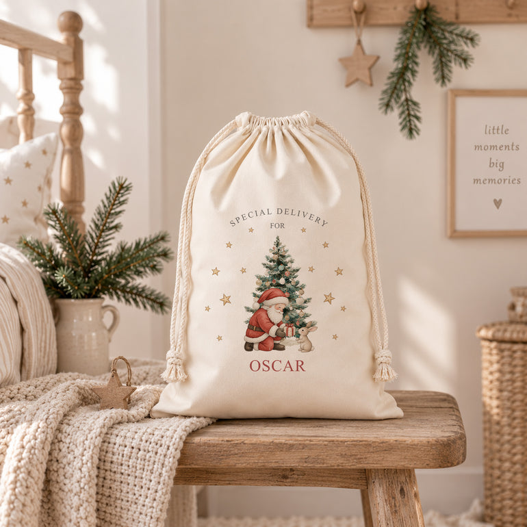 Large personalised Christmas Santa sack with child’s name, Santa and bunny Special Delivery design beside a festive Christmas tree.