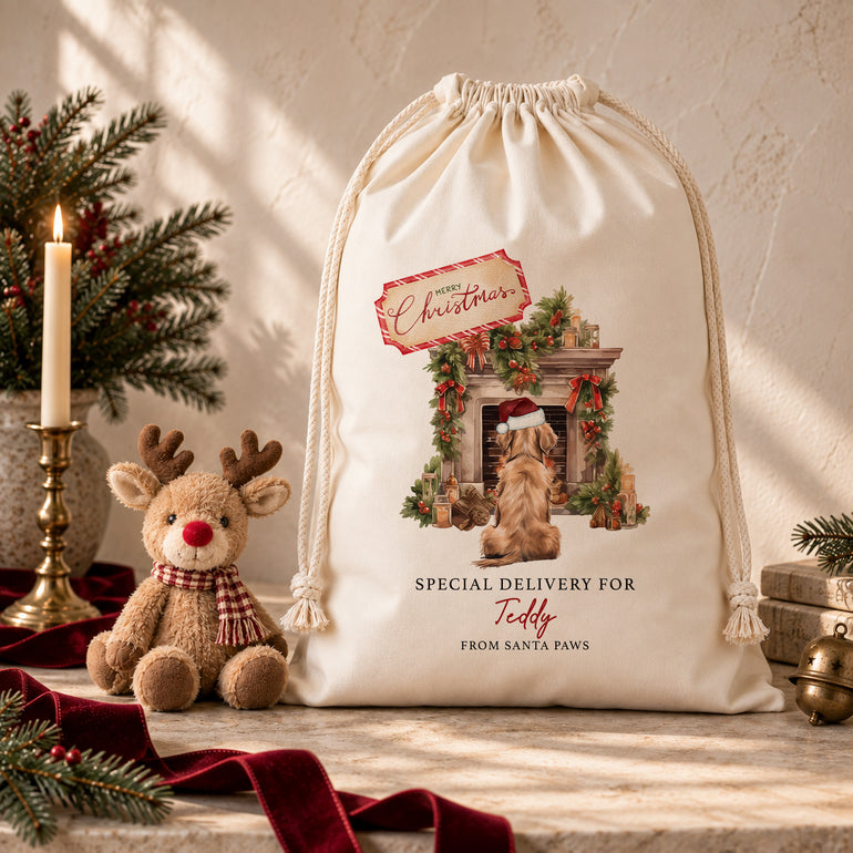 Santa Paws pet Christmas sack with a festive fireplace scene, displayed on a wooden bench beside a reindeer toy.