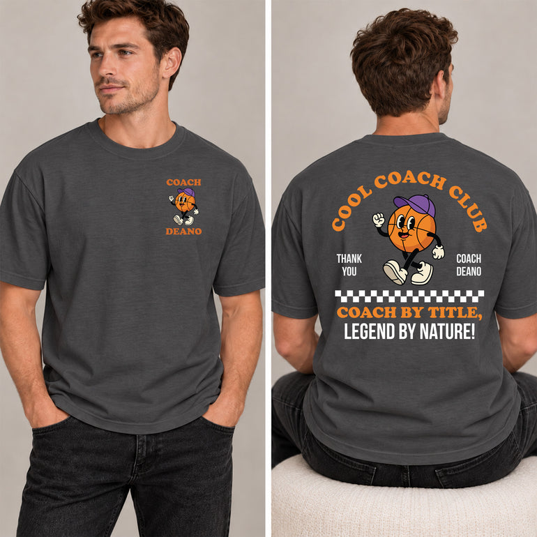 Man in a charcoal Cool Coach Club basketball coach gift T-shirt, the back printed with Cool Coach Club, a retro cartoon basketball character in a purple cap, Thank You, Coach Deano and Coach by Title, Legend by Nature, the front with a small Coach Deano badge