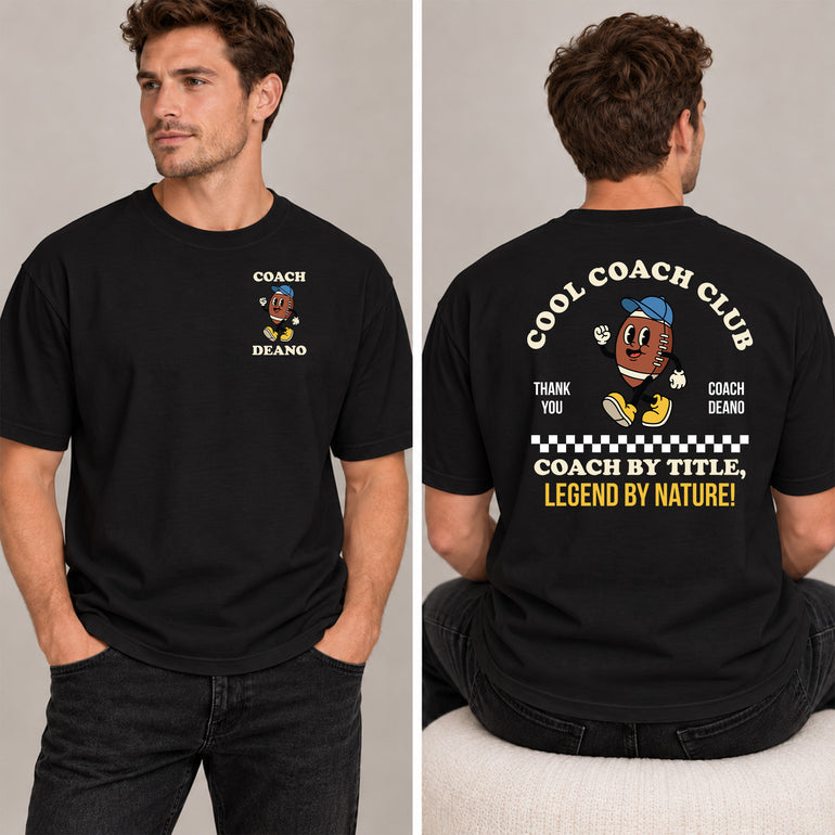 Man in a black Cool Coach Club rugby coach gift T-shirt, the back printed with Cool Coach Club, a retro cartoon rugby ball character in a blue cap, Thank You, Coach Deano and Coach by Title, Legend by Nature, the front with a small Coach Deano badge