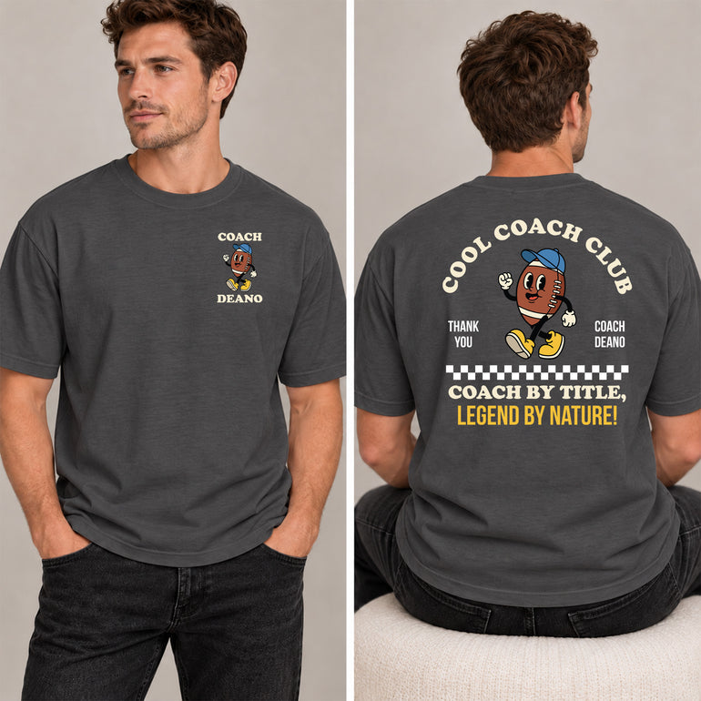 Man in a charcoal Cool Coach Club rugby coach gift T-shirt, the back printed with Cool Coach Club, a retro cartoon rugby ball character in a blue cap, Thank You, Coach Deano and Coach by Title, Legend by Nature, the front with a small Coach Deano badge