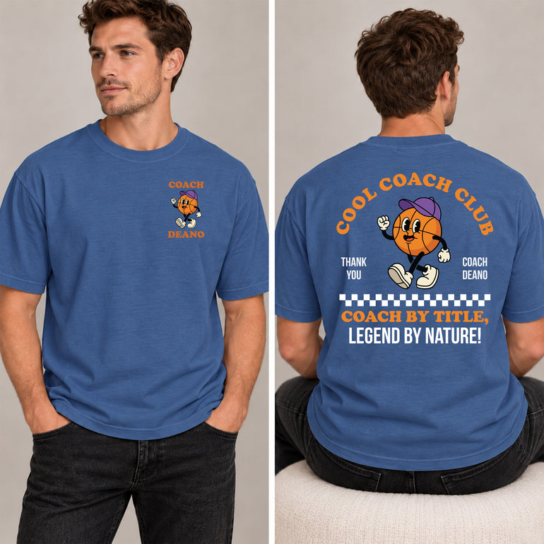 Man in an indigo blue Cool Coach Club basketball coach gift T-shirt, the back printed with Cool Coach Club, a retro cartoon basketball character in a purple cap, Thank You, Coach Deano and Coach by Title, Legend by Nature, the front with a small Coach Deano badge
