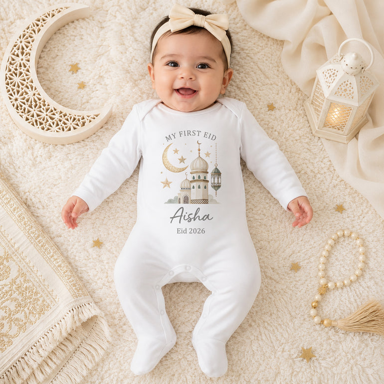Baby wearing a neutral personalised First Eid baby grow with mosque, crescent moon, lantern and name design on a cream Eid background.