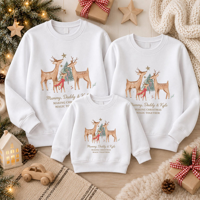Three white matching family Christmas jumpers laid flat among festive decorations, with the reindeer family design and example names in gold