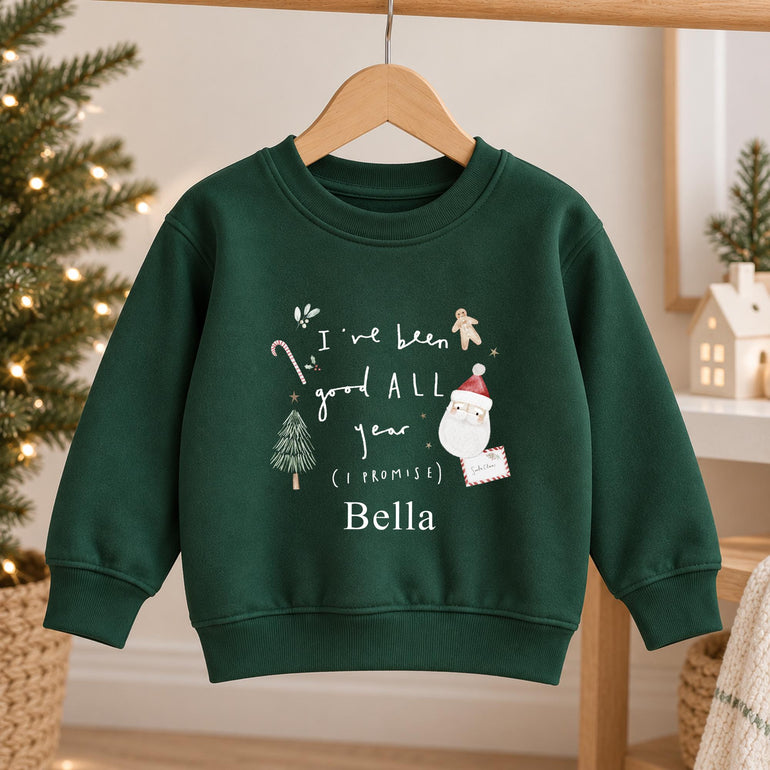 Forest green kids Christmas jumper on a wooden hanger with I've been good ALL year (I promise), Santa, a letter to Santa, a candy cane, a gingerbread man and a tree, personalised with a name in white