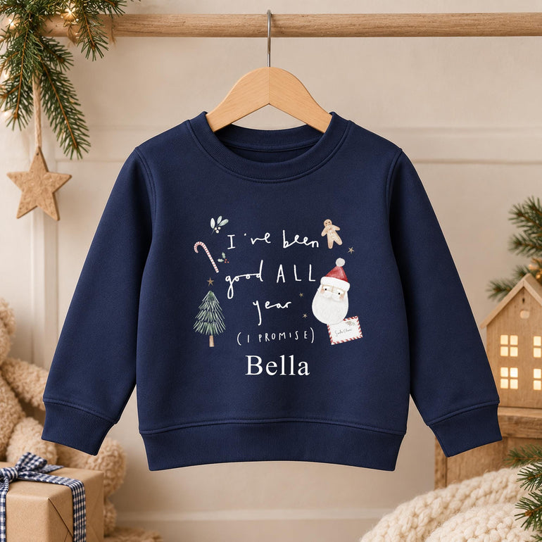 Navy personalised kids Christmas jumper on a hanger with white hand-lettered I've been good ALL year wording, a watercolour Santa and a name