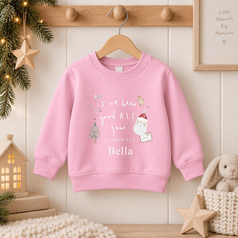 Light pink kids Christmas jumper hanging on a peg rail, with Santa, a gingerbread man and I've been good ALL year (I promise) above a name