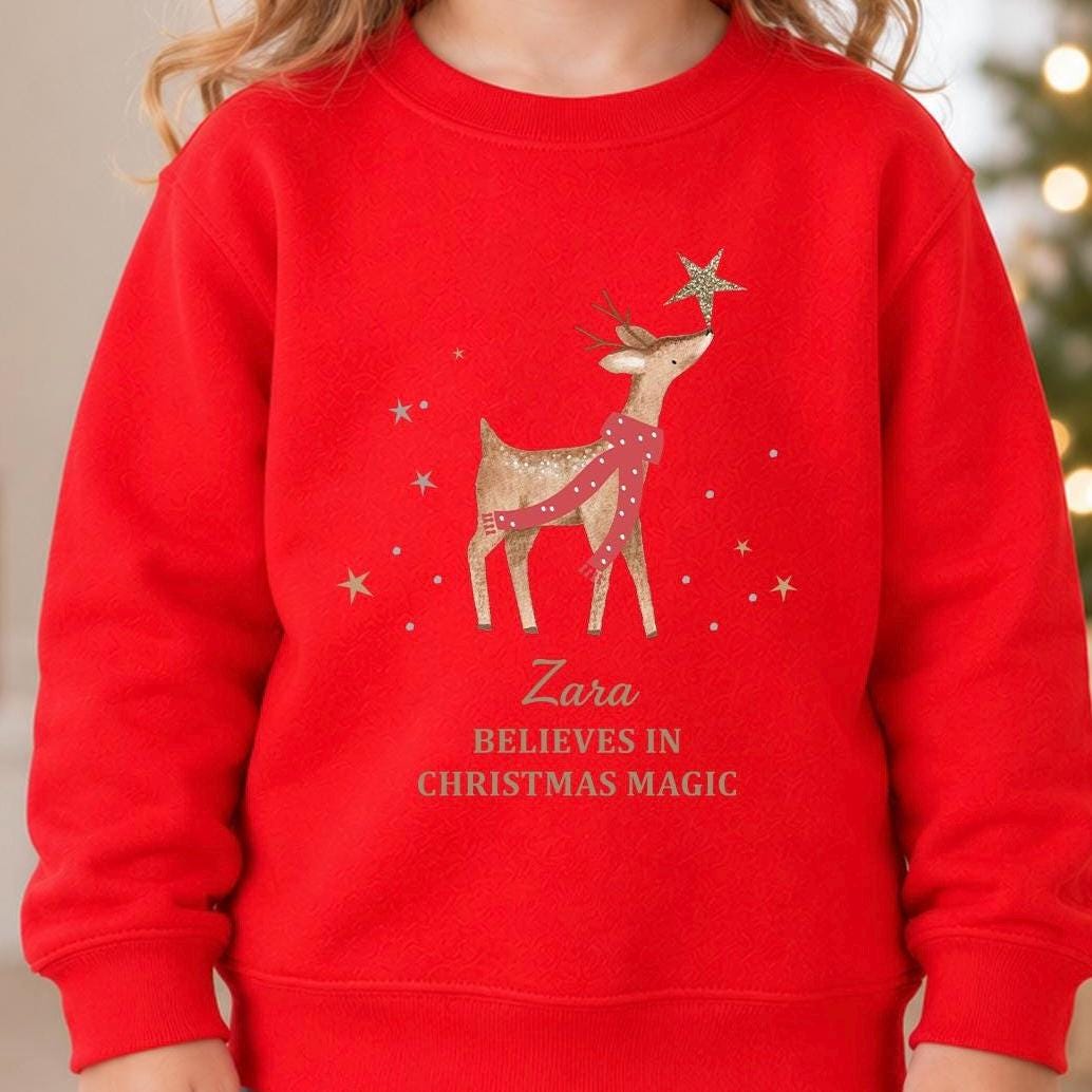 Red personalised reindeer Christmas jumper with a reindeer touching a gold star, a child's name in gold script and Believes in Christmas Magic
