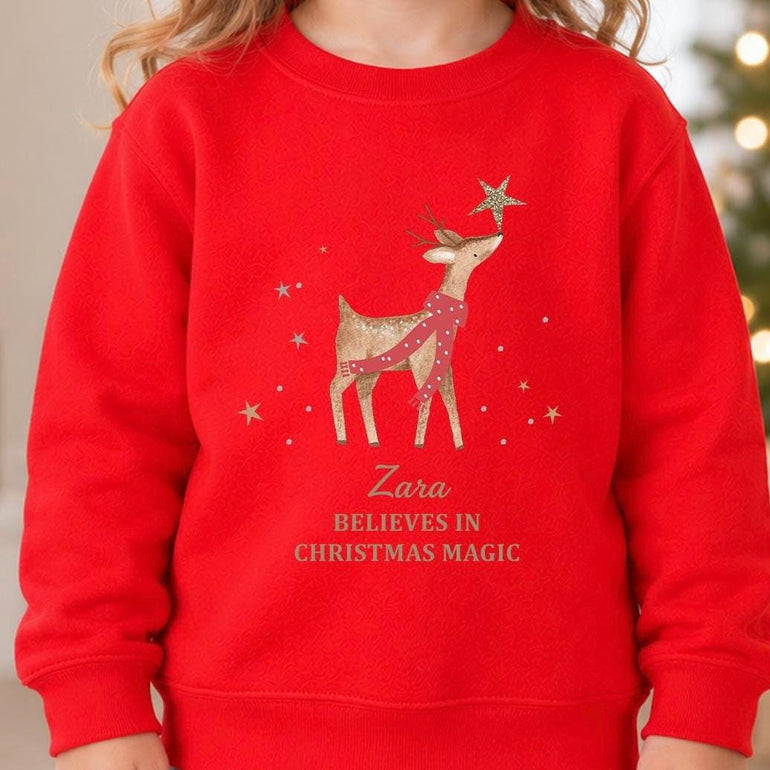 Red personalised reindeer Christmas jumper with a reindeer touching a gold star, a child's name in gold script and Believes in Christmas Magic