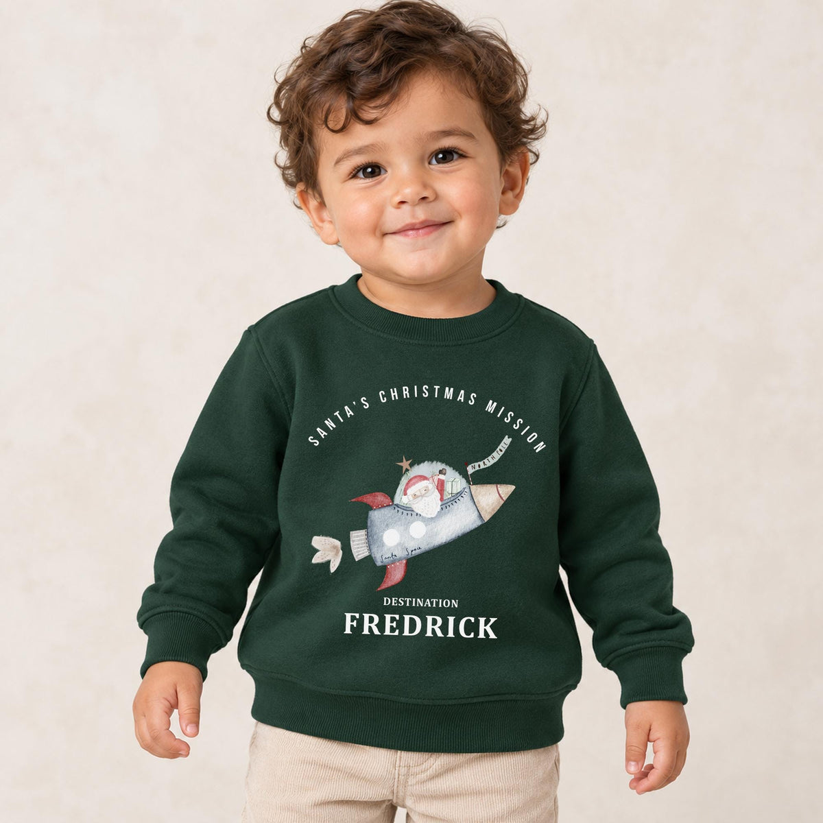 Toddler wearing a forest green personalised space Christmas jumper with Santa flying a rocket and a name beneath
