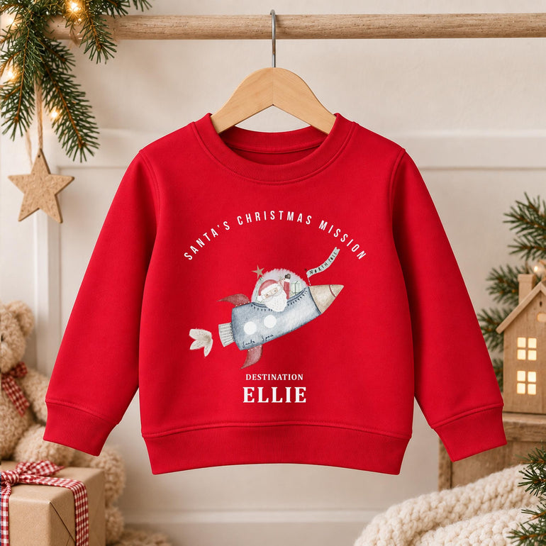 Red kids space Christmas jumper on a hanger with Santa flying a rocket and a name in white