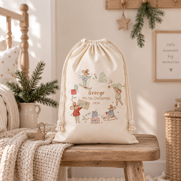 Cream winter mice first Christmas sack on a wooden bench with a knitted blanket in a softly styled festive room.