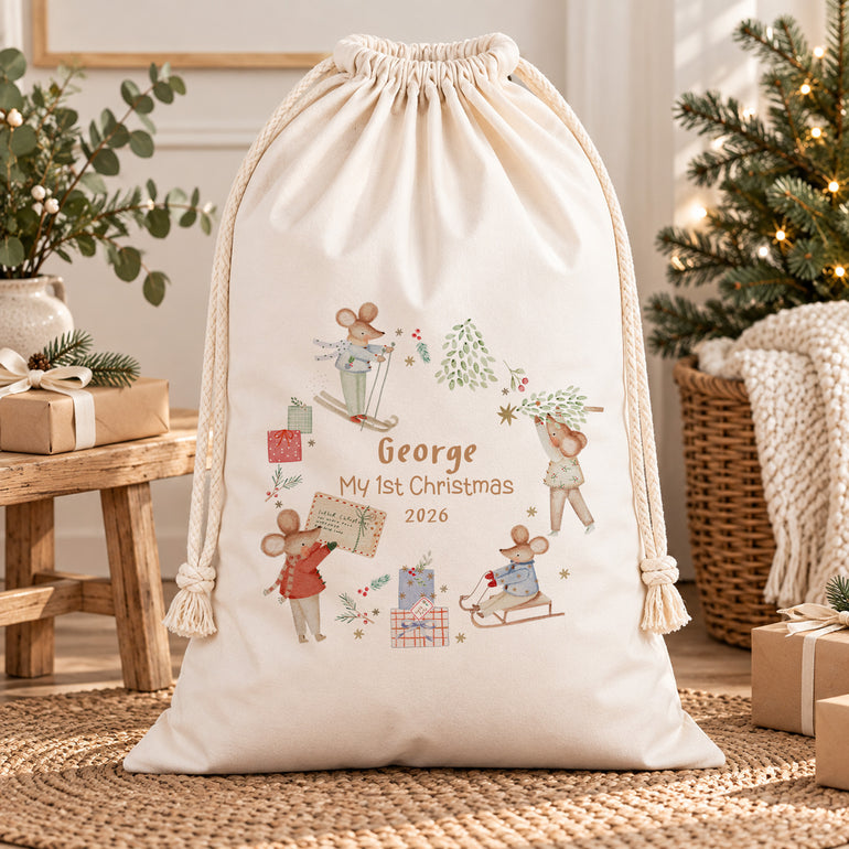 Winter mice baby’s first Christmas sack personalised with a name and year, shown beside a wooden table and greenery.