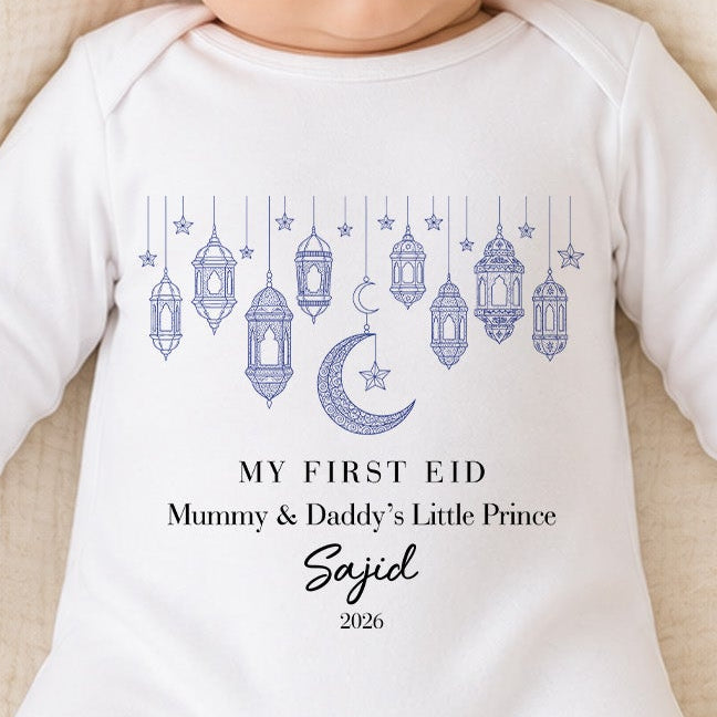Baby in a white onesie with 'My First Eid' text, lying in a woven basket.