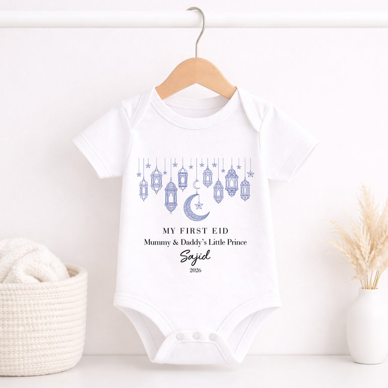 White baby onesie with 'My First Eid' design on a wooden hanger against a white background.