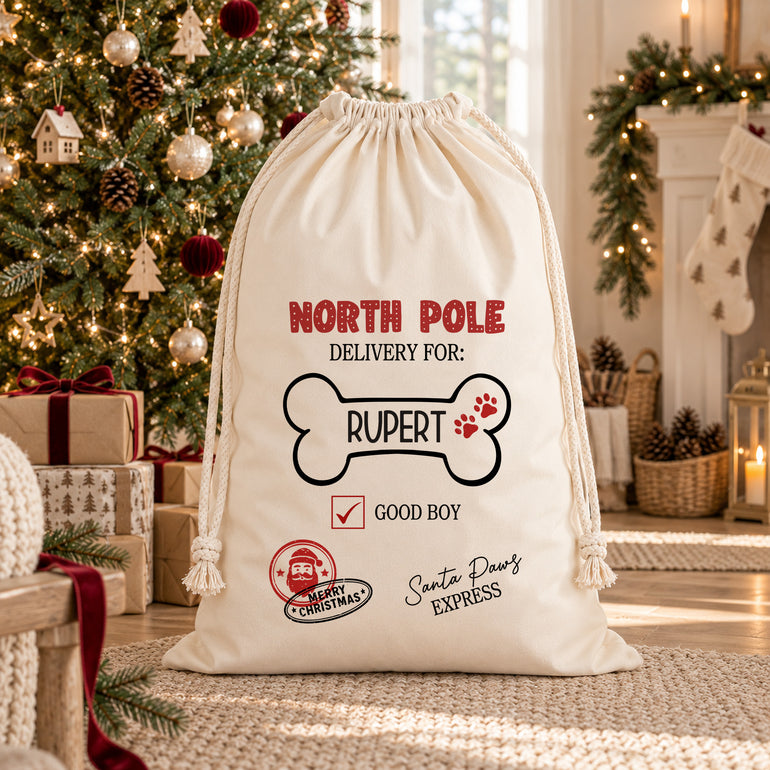 Cream dog Christmas sack personalised with Rupert inside a bone outline, with North Pole lettering and a Good Boy checkbox, beside a decorated tree.
