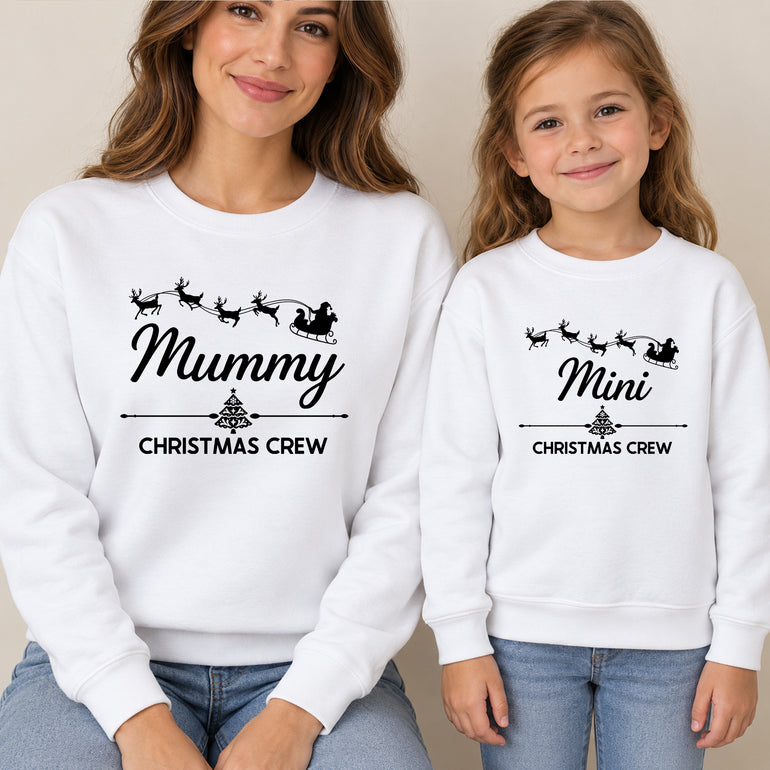 Mum and daughter in matching white Christmas jumpers reading Mummy Christmas Crew and Mini Christmas Crew with Santa's sleigh and reindeer