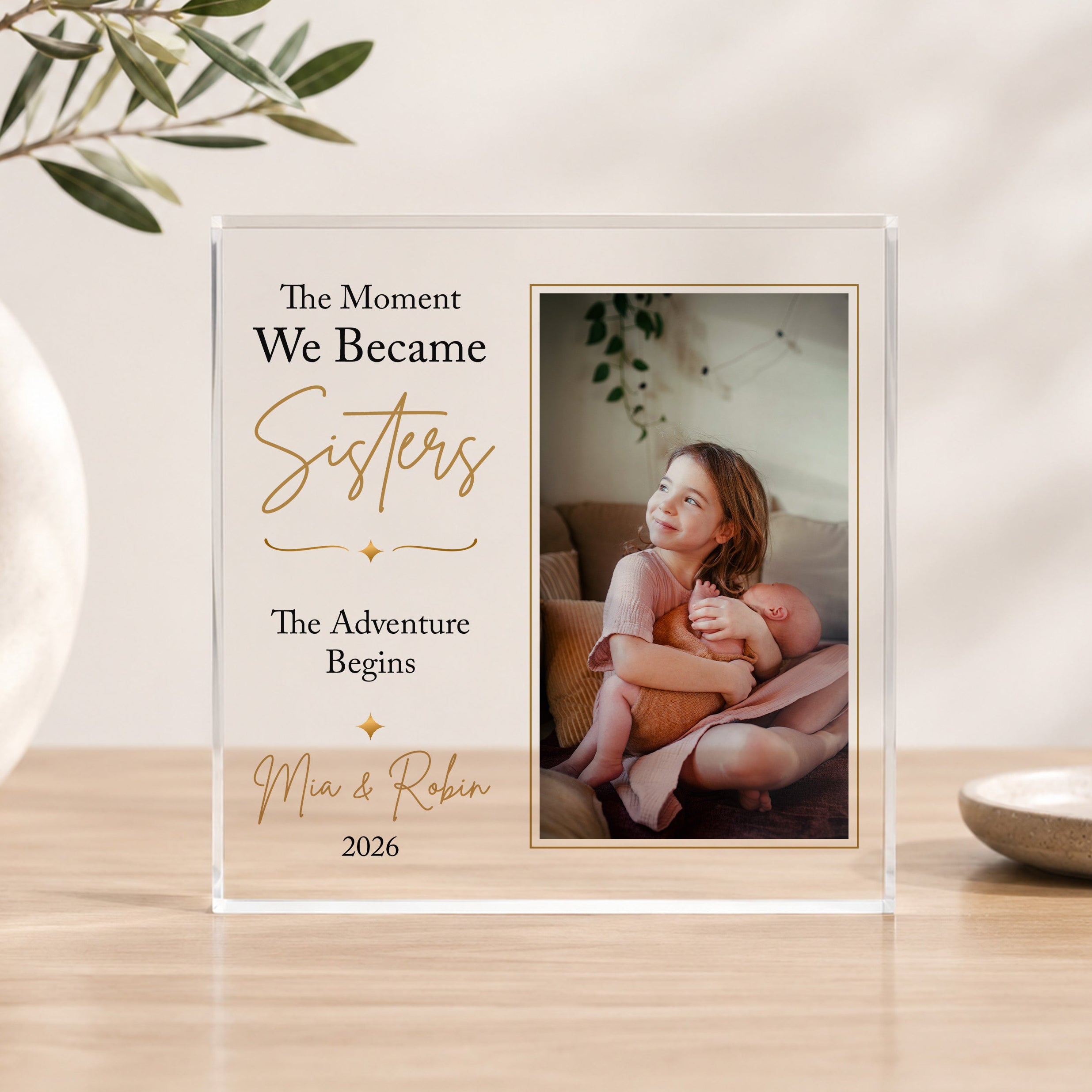 Personalised new sisters acrylic photo block showing big sister cuddling her newborn baby sister with custom names and year.