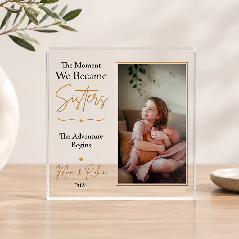 Personalised new sisters acrylic photo block showing big sister cuddling her newborn baby sister with custom names and year.