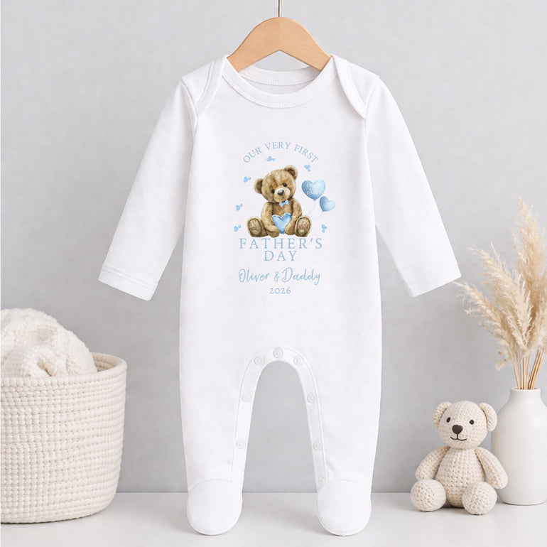 White baby grow 1st Father's Day with teddy bear design on a hanger against a light gray background.